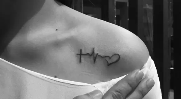Tatuaż linia życia na ramieniu: krzyż, EKG i serce. Symbol wiary, życia i miłości.