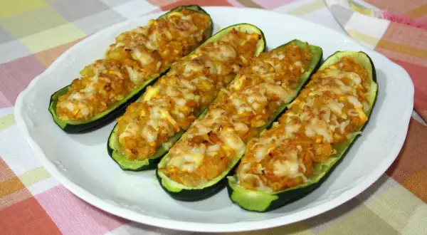 Cuatro calabacines rellenos, gratinados con queso, servidos en un plato blanco sobre un mantel a cuadros.