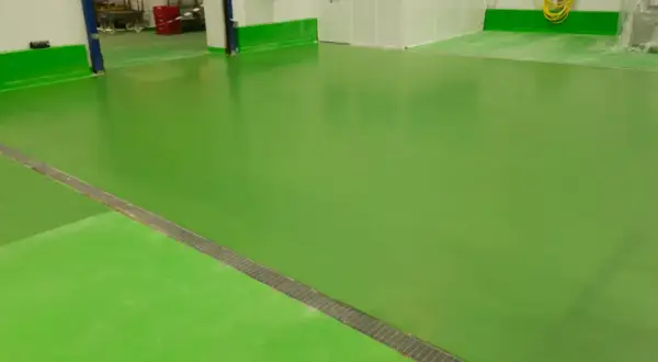Suelo de nave industrial de color verde brillante, con un desagüe metálico en diagonal.