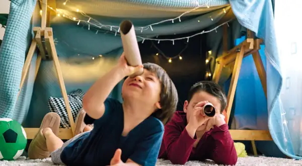 Zwei Jungen erkunden in einer gemütlichen Höhle mit Lichterketten ihre Welt. Perfekte Spiele ab 3 Jahre für fantasievolle Abenteuer.