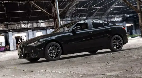 Czarny Alfa Romeo Giulia Quadrifoglio w opuszczonej hali przemysłowej.