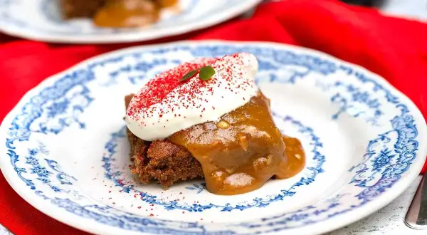 En bit saftig sockerkaka med pepparkakskrydda, toppad med vispad grädde och strössel. Serveras på en vacker blåvit tallrik.