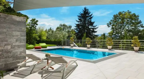 Moderne poolumrandungen ideen: ein rechteckiger Pool mit türkisfarbenem Wasser, umgeben von hellen Terrassenplatten, Liegestühlen und grünen Sitzsäcken.