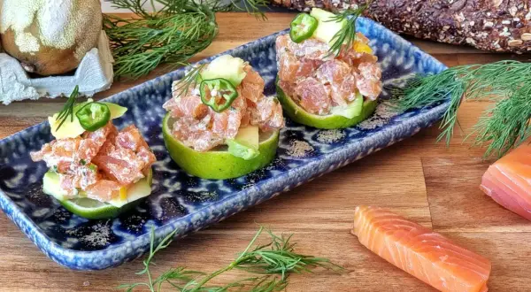 Delicioso tartar de salmón y aguacate servido en mitades de lima, decorado con jalapeño y eneldo.