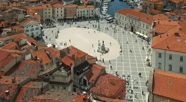 Widok na plac w Piran, Słowenia, z widokiem na morze i port. Czerwone dachy i zabytkowa architektura tworzą malowniczy krajobraz.