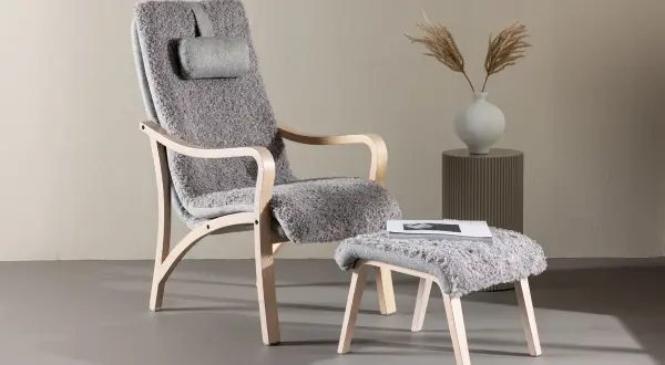En bekväm trä fåtölj med grå fårskinnsklädsel och en matchande pall. Perfekt för en mysig läshörna.