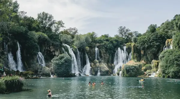 Atemberaubende Wasserfälle in Bosnien, Natur pur. Menschen genießen das kühle Wasser in einem türkisfarbenen See, umgeben von üppiger Vegetation.