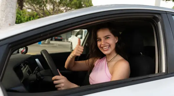 Joven sonriente en coche, pulgar arriba. ¡Ya sabe hasta que edad se puede conducir en España!