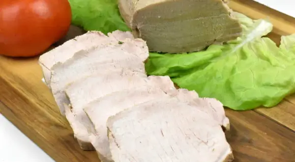 Pokrojony schab gotowany w majonezie, liście sałaty i pomidor na desce.