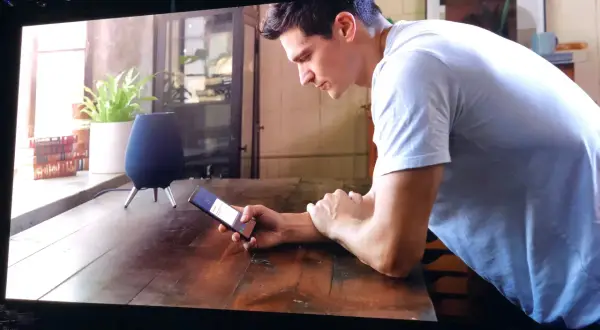 Un homme utilise son téléphone pour contrôler son **galaxy home**. Un haut-parleur intelligent est visible sur la table.