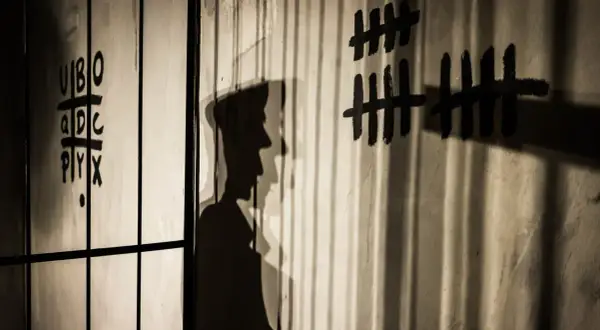 Shadows cast by bars and a figure on a wall with tally marks and letters. This image illustrates how to avoid shadows in indoor photography by using them creatively.