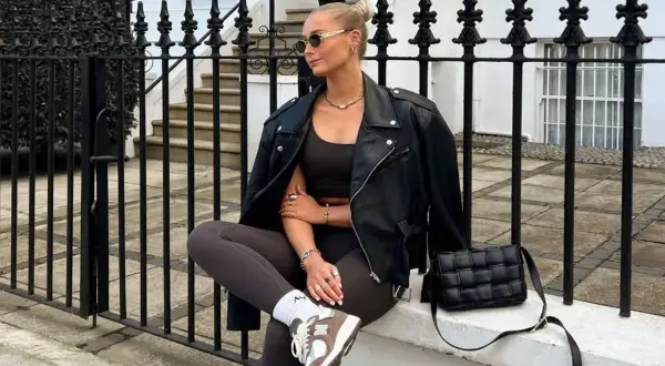 Kobieta w czarnej ramonesce, brązowym topie i legginsach, prezentująca styl athleisure. Obok czarna, pikowana torebka.
