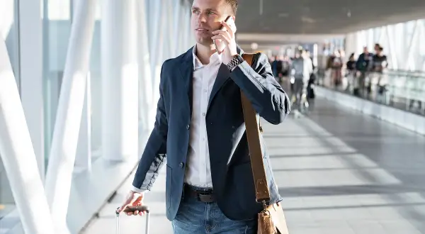 Mężczyzna w marynarce rozmawia przez telefon, ciągnąc walizkę. Może to być podróż służbowa, o której mowa w art. 21 ust. 1 pkt 152 ustawy o podatku dochodowym.