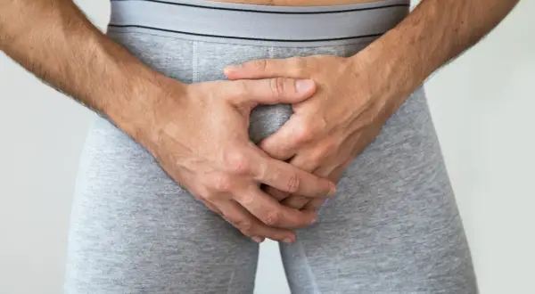 Mężczyzna w szarych bokserkach, ręce skrzyżowane na kroczu. Dyskretne pytanie: jak powiększyć kutasa?