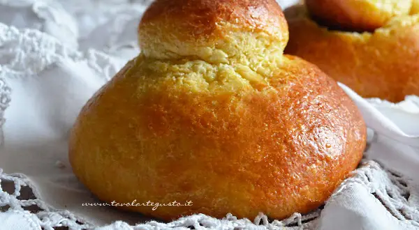Brioches siciliane ricetta originale con strutto, dorate e soffici, su un pizzo bianco.