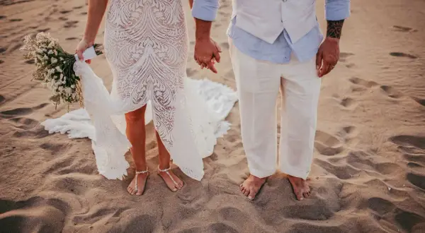 Coppia felice in un matrimonio spiaggia. La sposa con un bouquet, lo sposo con un gilet leggero.