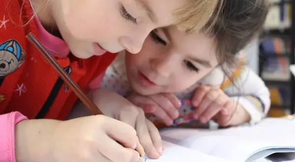 Zwei Kinder lernen gemeinsam an einer Lerntheke Methode, konzentriert auf ihr Heft.