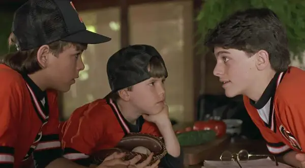 Trzej chłopcy w strojach baseballowych, przypominający scenę z filmów dla dzieci z lat 90. Jeden z nich trzyma rękawicę z piłką.