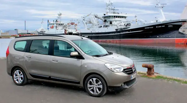 Brązowy Dacia Lodgy zaparkowany przy nabrzeżu, w tle wielkie statki rybackie.