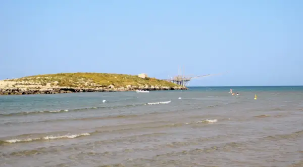 La chianca di Vieste, con la sua struttura in legno sul mare, si staglia contro il cielo azzurro. L'acqua cristallina invita a un bagno rinfrescante.