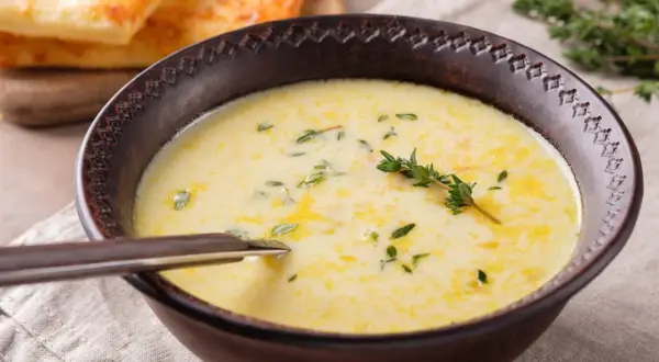 A creamy zupa na rosole, garnished with fresh thyme, served in a rustic bowl with a spoon. In the background, golden-brown toasted bread.