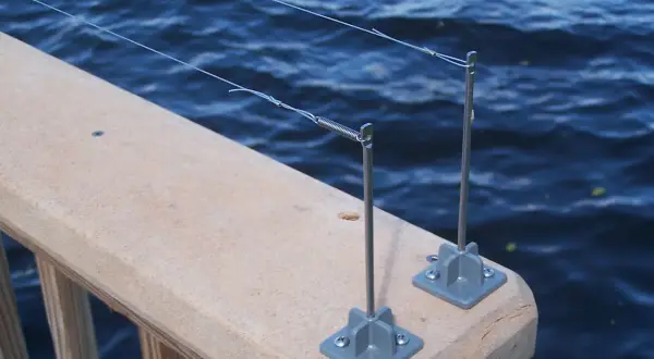 Deux piquets de pêche sur un garde-corps en bois, prêts à attraper un poisson. L'eau bleue ondule derrière.