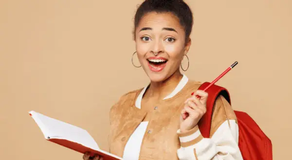 Jeune femme souriante avec un livre et un crayon, prête pour sa lettre de motivation stage à l'étranger.