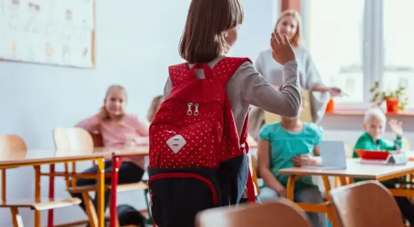 Dziewczynka z czerwonym plecakiem w klasie, może odczuwać lęki u dziecka 7 latka, ale nauczycielka i koledzy dodają jej otuchy.