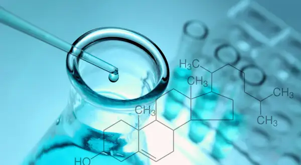 Pipeta z kroplą płynu nad kolbą, probówki i wzór chemiczny cholesterolu.