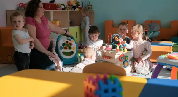 W przedszkolu opiekunka dba o kilkoro dzieci bawiących się zabawkami.