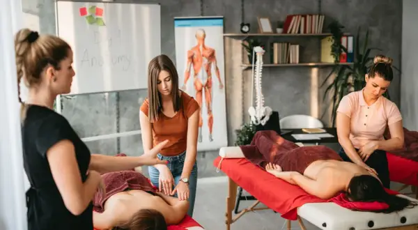 Insegnante mostra a studenti chi fa i massaggi, con diagrammi anatomici sullo sfondo.