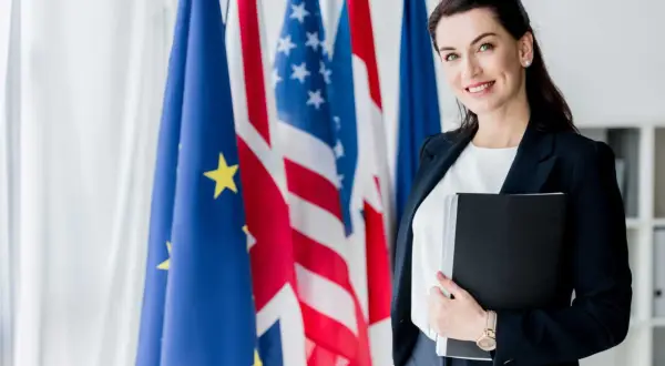 Donna sorridente con cartella, sullo sfondo bandiere UE, USA e Francia. Un futuro in scienze investigative triennale.