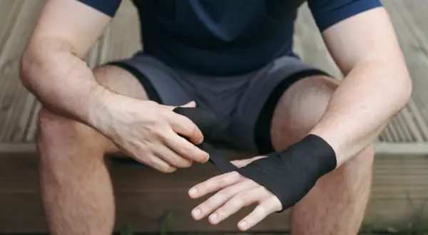 A boxer wraps his hands, ensuring the wraps are snug but not too tight. This is key to protecting his knuckles and wrists during a fight.