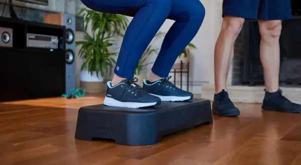 Person macht Kniebeugen auf einer Aerobic-Plattform. Die **step aerobic schuhe** sind dunkelblau mit hellblauen Akzenten.