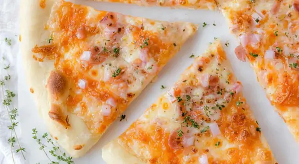 Kawałki pysznej pizzy bez drożdży z ciągnącym się serem, szynką i cebulką, posypane świeżym tymiankiem.