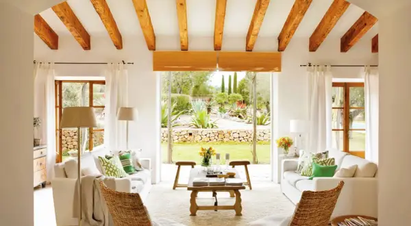 Salón con vigas de madera y vistas a un jardín exuberante, reflejo de la arquitectura mediterránea.