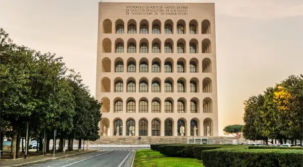Il Colosseo Quadrato, imponente edificio con arcate sovrapposte, si erge maestoso tra alberi verdi e un cielo tenue.