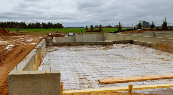Fundament betonowy w budowie, z widocznymi zbrojeniem i folią. Trudno oszacować ile bloczków betonowych na fundament zużyto.