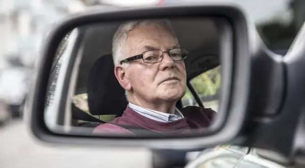 Älterer Mann mit Brille im Rückspiegel, der sich fragt, warum das Auto quietscht.