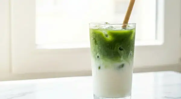 Un cocktail matcha glacé, avec du lait et une paille en bambou, sur un fond lumineux.