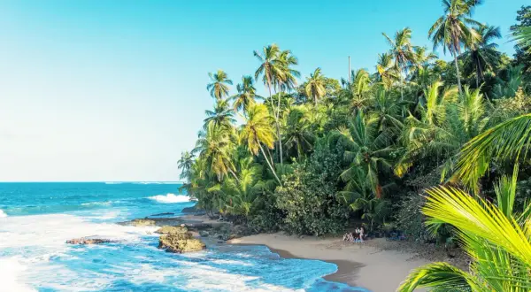 En tropisk strand i Costa Rica med vajande palmer, turkost hav och en liten grupp människor som njuter av solen.