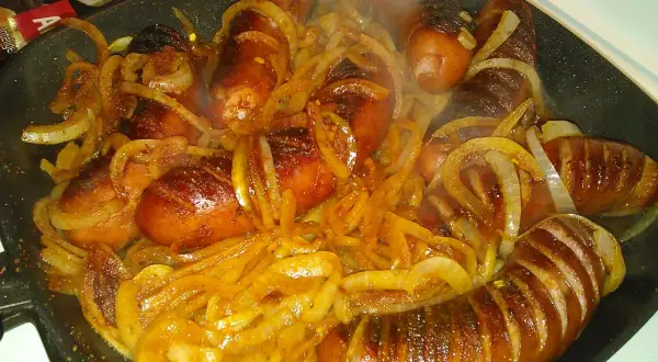 Gorąca kiełbasa z cebulą skwierczy na patelni, tworząc apetyczny aromat.
