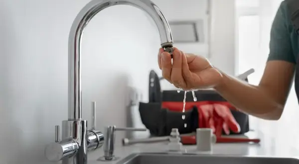 Instrukcja, jak usunąć kamień z kranu: hydraulik pokazuje wyczyszczony aerator, z którego kapie woda. W tle torba z narzędziami.