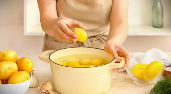 Hände legen Kartoffeln in einen Topf mit Wasser. Die Kochzeit für Kartoffeln beginnt jetzt.