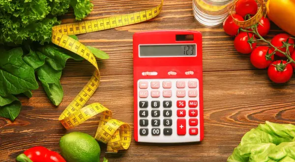 Czerwony kalkulator obok miarki i świeżych warzyw. Zastanawiasz się, ile to kcal? Oblicz swoją dietę!