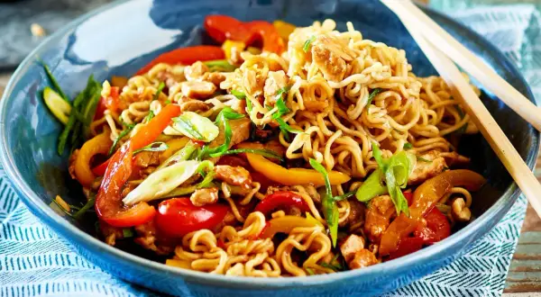 Schüssel mit Nudeln, Paprika, Frühlingszwiebeln und Hühnchen. Ein Teller mit einfachen asiatischen Gerichten, bereit zum Genießen mit Stäbchen.