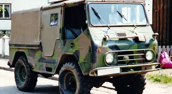 En kamouflerad Volvo L3314 står parkerad framför ett hus.