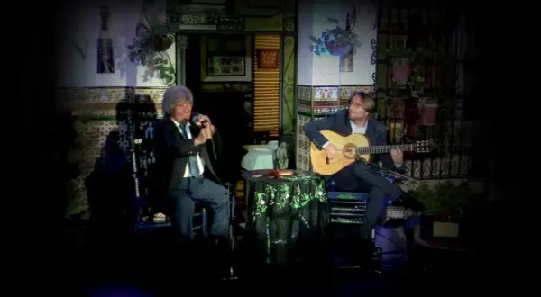 Dos hombres disfrutan de un emotivo canto flamenco. Uno canta al micrófono, el otro acompaña con su guitarra.
