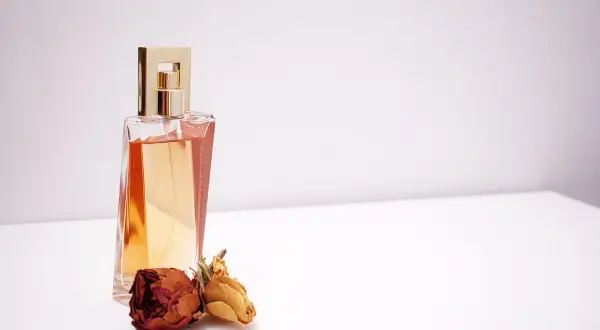 Elegancka butelka perfum z płynem w kolorze bursztynu, obok niej dwie zasuszone róże. Czy to piżmo co to za nuta zapachowa?