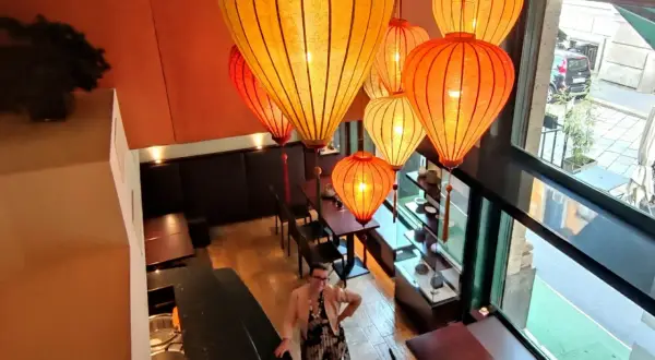 Interno di un ristorante cinese a Milano, illuminato da lanterne orientali. Una donna osserva l'ambiente.